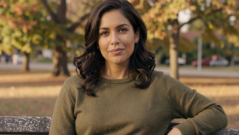 Approachable woman in olive sweater on a park bench representing authentic dating profile imagery